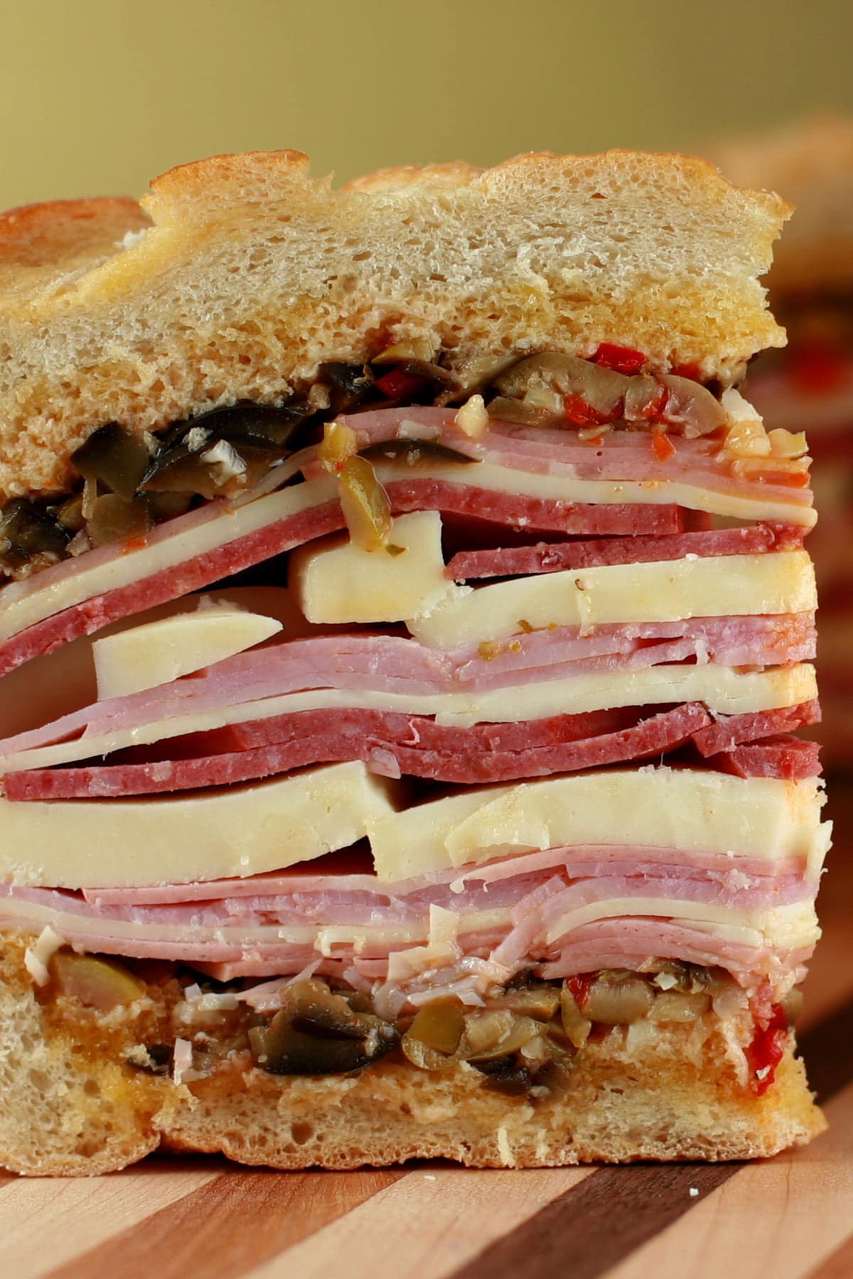 A large wedge of muffaletta sandwich: A full loaf of bread, stuffed with many layers of meats, cheeses, and olive salad.