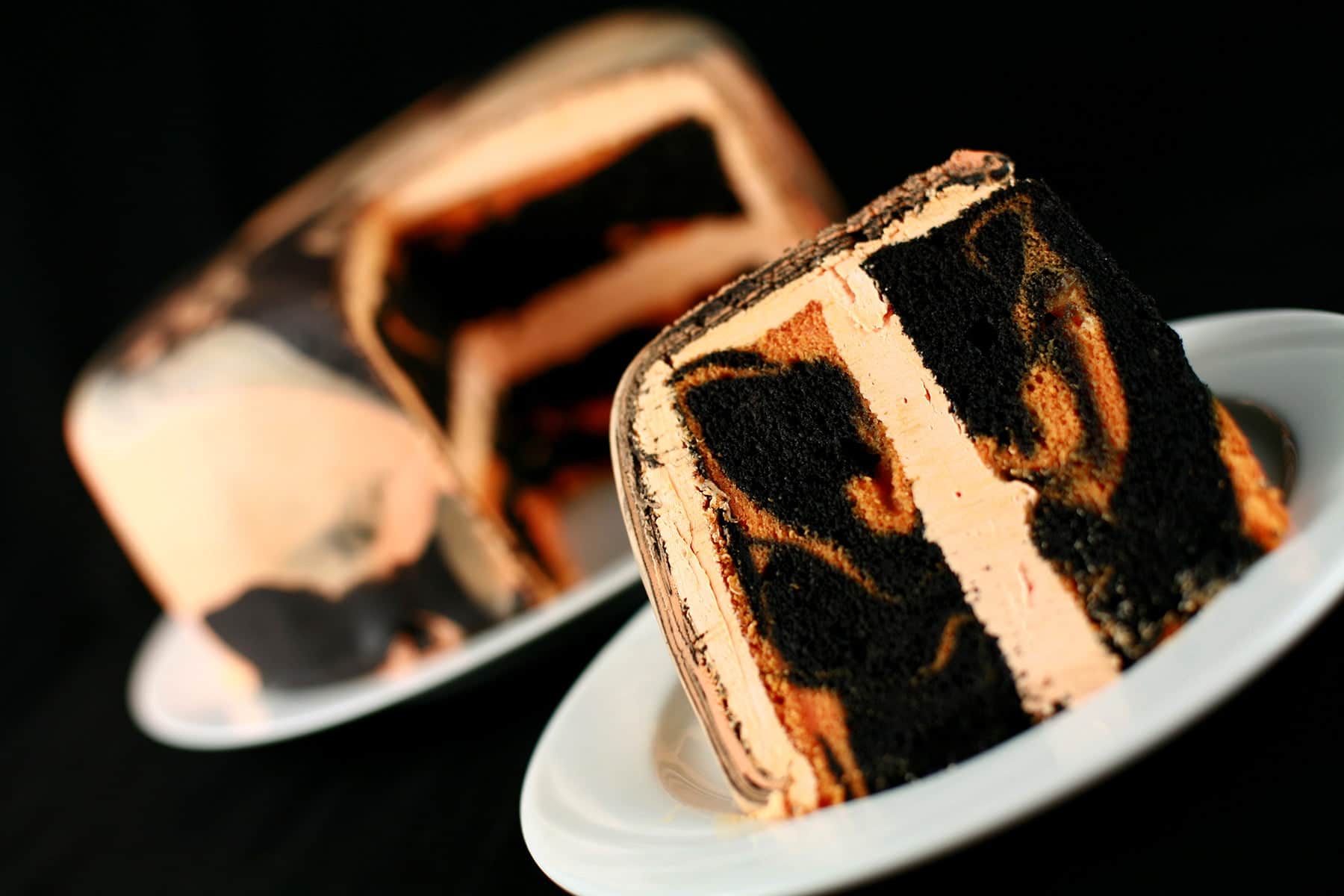 A large round tiger tail cake - black licorice and orange marbled cake, with orange buttercream - is shown with a slcie cut out, and served on a plate in front of it.