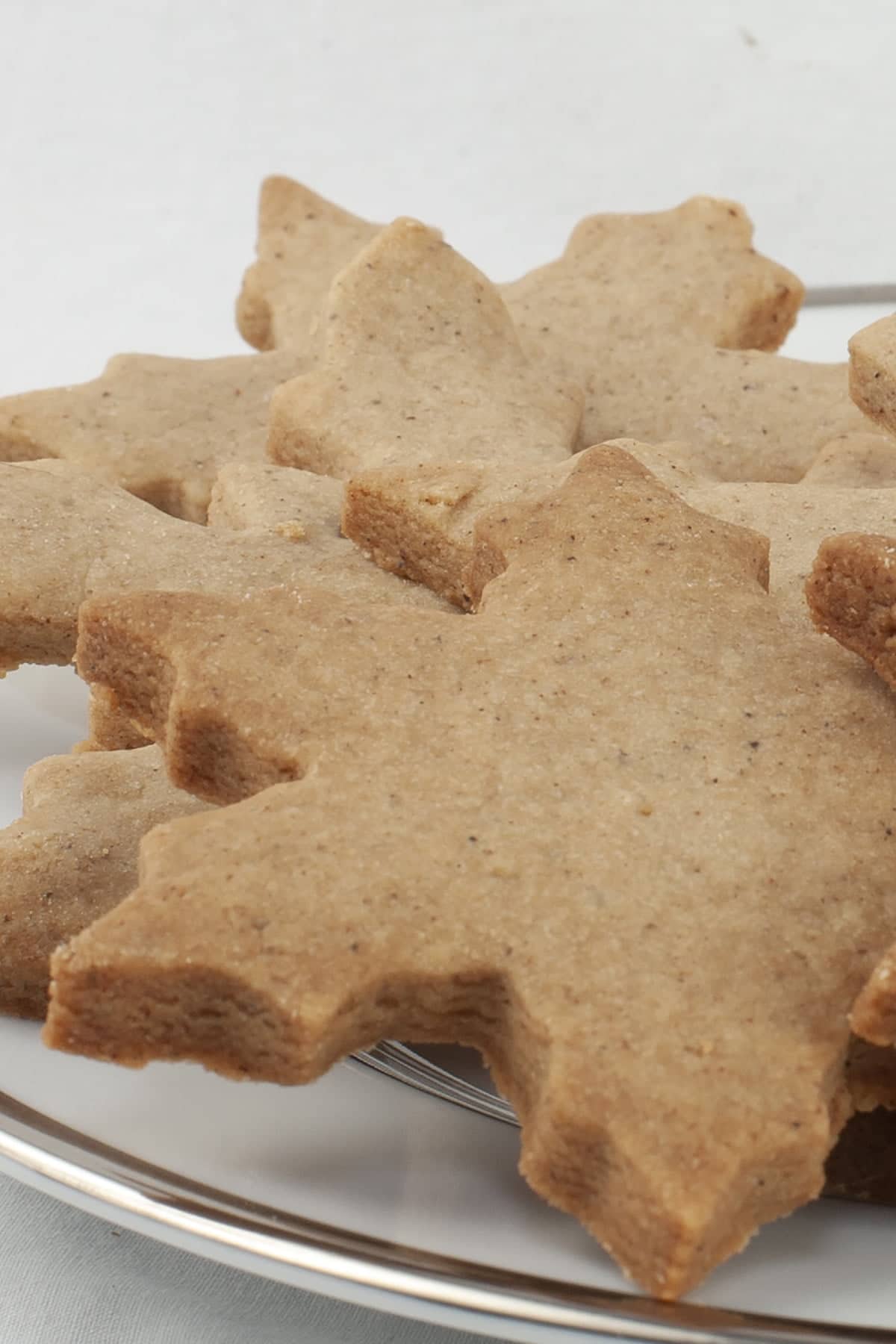 A pile of golden brown shortbread cookies - shaped like snowflakes - are piled on a small white plate.