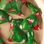 6 different Chocolate Zombie Easter Bunnies are arranged on a beige coloured oval plate. They're all green woth red, white, and brown designs to make them look blood spattered, scarred, etc.