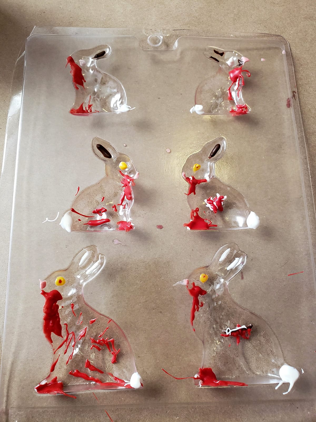 A plastic bunny mold with some of the designs filled in with brightly coloured melted candy.