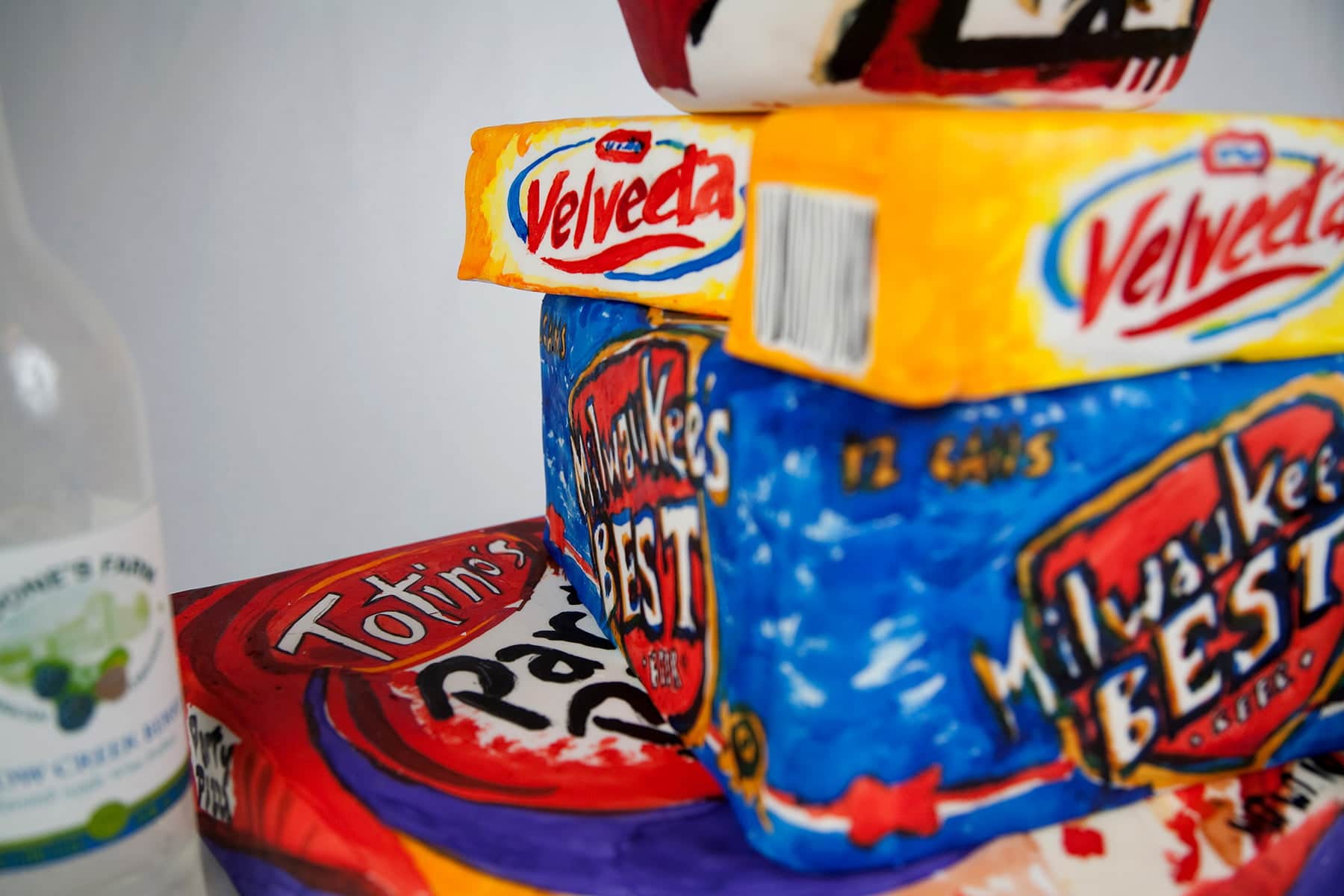 A cake made up of layers and side pieces to look like a Totino's box, a "Milwaukee's Best" case of beer, bricks of Velveeta, a bucket of KFC, a canister of spray cheese, and 2 empty bottles of Boone's Farm. Everything is hand painted with food colouring.
