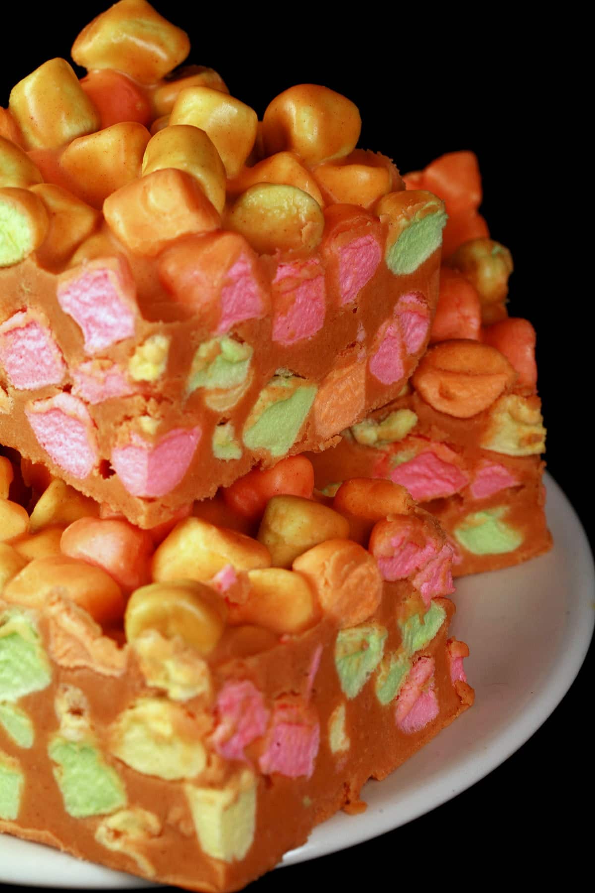A white plate is stacked with Confetti Bars - rainbow marshmallows held together with butterscotch fudge.