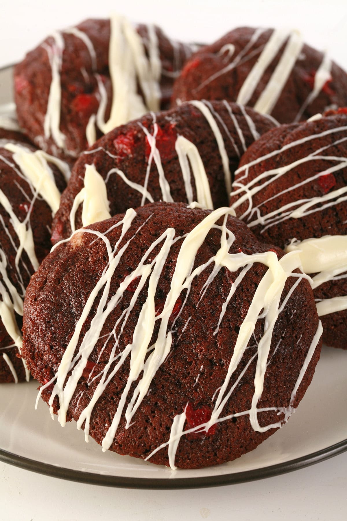 A plate of chewy black forest cookies, studded with bits of maraschino cherry and drizzled in white chocolate.
