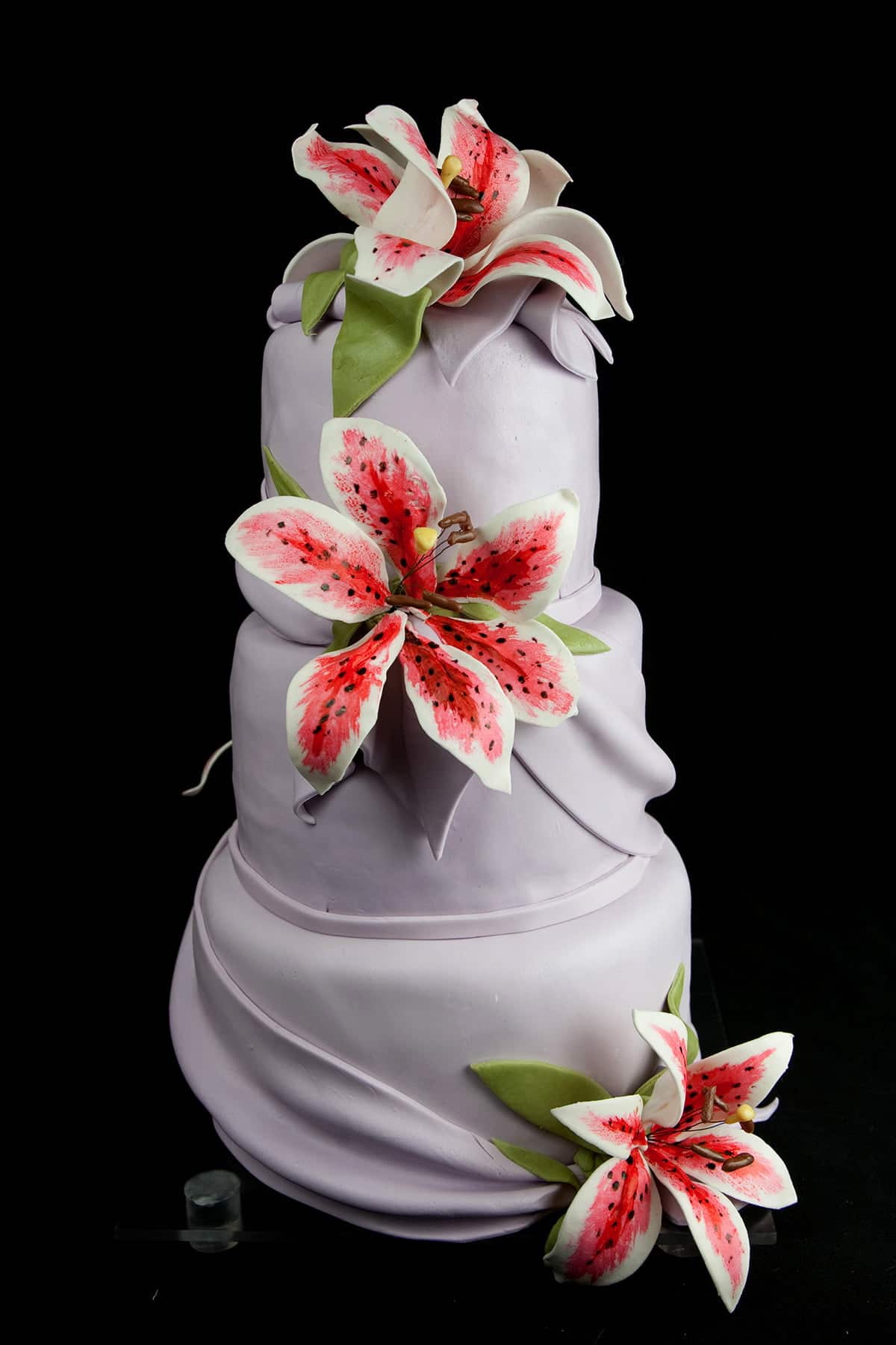 A 3 tiered purple wedding cake. The cake is covered in lavender fondant, and features swags of matching fondant and sugar Stargazer Lilies.