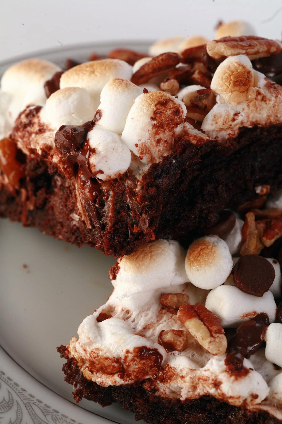 A close up view of two rocky road brownies - double chocolate walnut brownies with toasted mini marshmallows, chocolate chips, and chopped pecans on top.