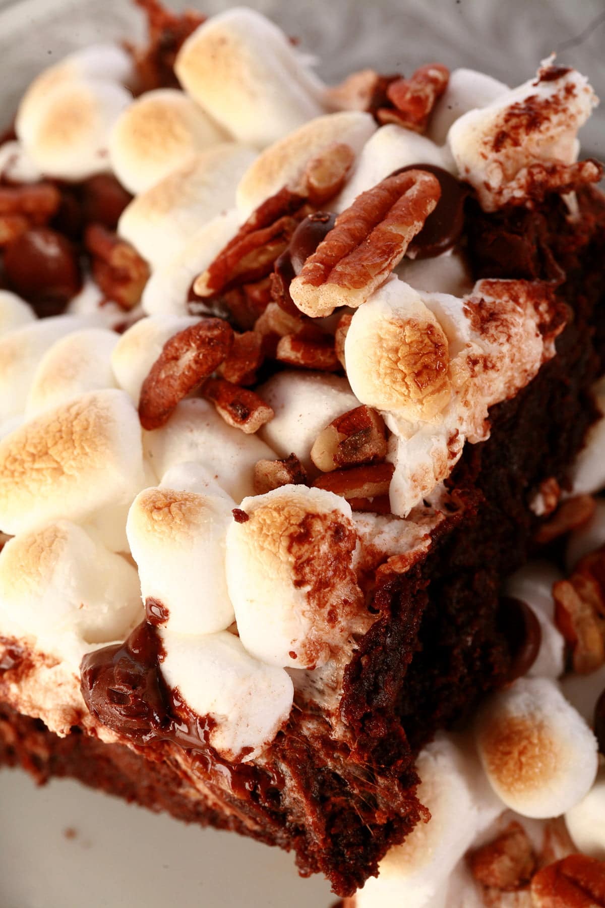A close up view of two rocky road brownies - double chocolate walnut brownies with toasted mini marshmallows, chocolate chips, and chopped pecans on top.