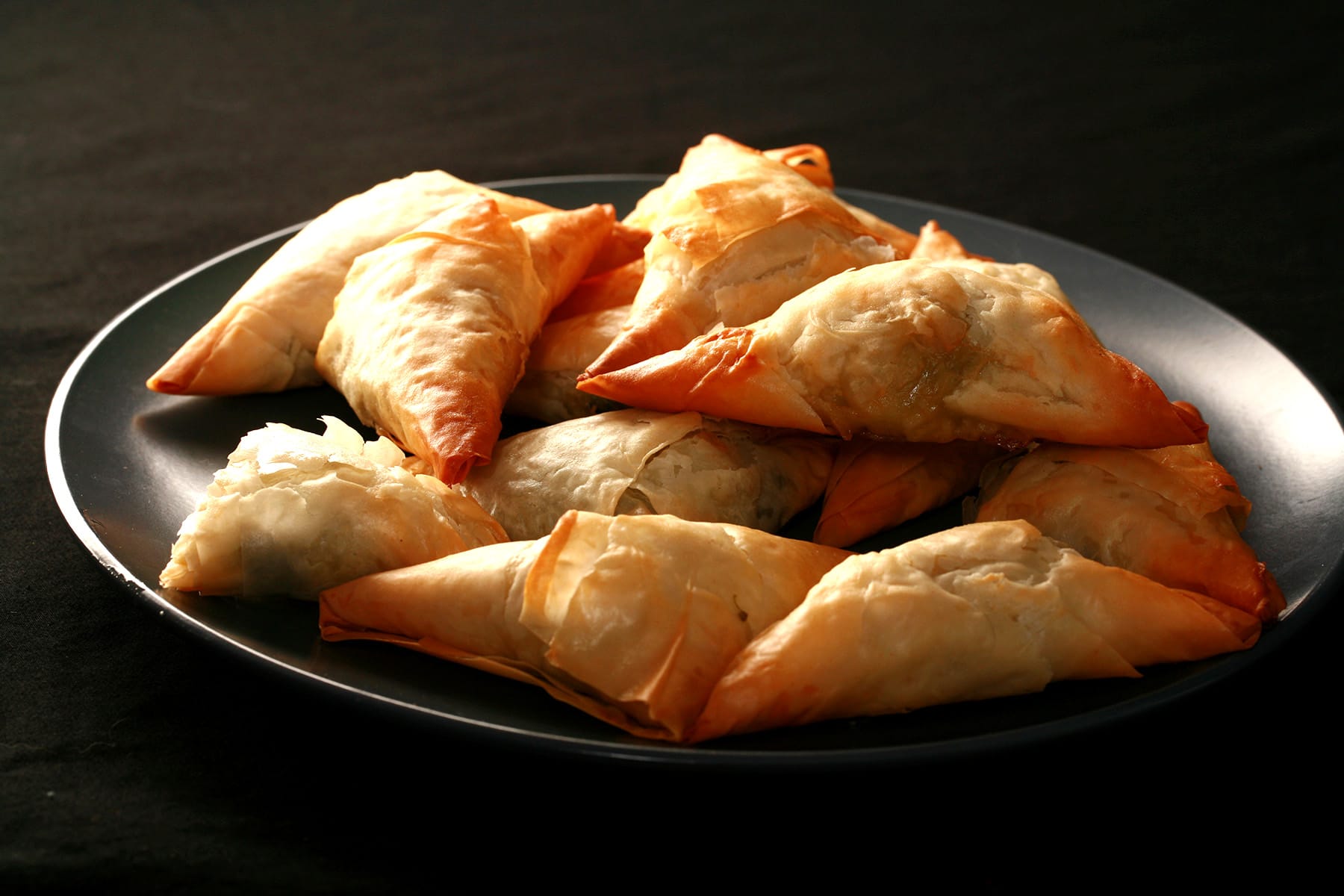 A small blue plate is piled with flaky Spanakopita Triangles.