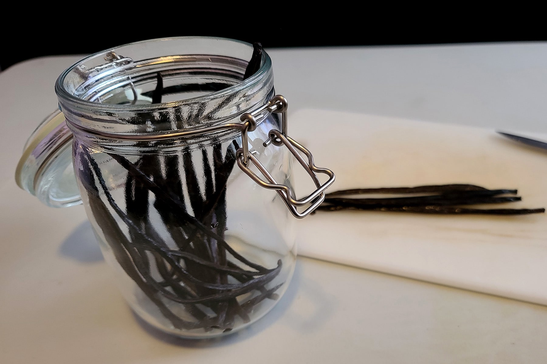 A glass jar with several split vanilla beans in it.