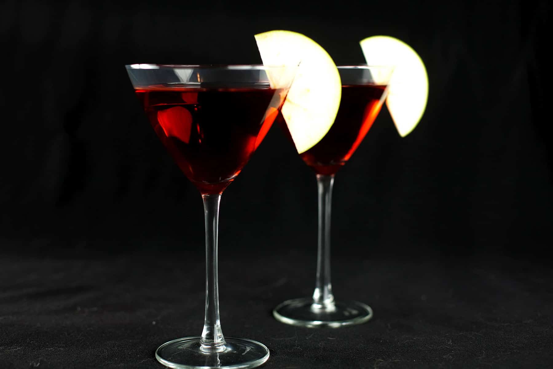 Two Candy Apple Martinis - large martini glasses are filled with a red liquid, and garnished with apple slices.
