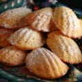 A small pile of sugar dusted Limoncello Madeleines, on a napkin lined plate.