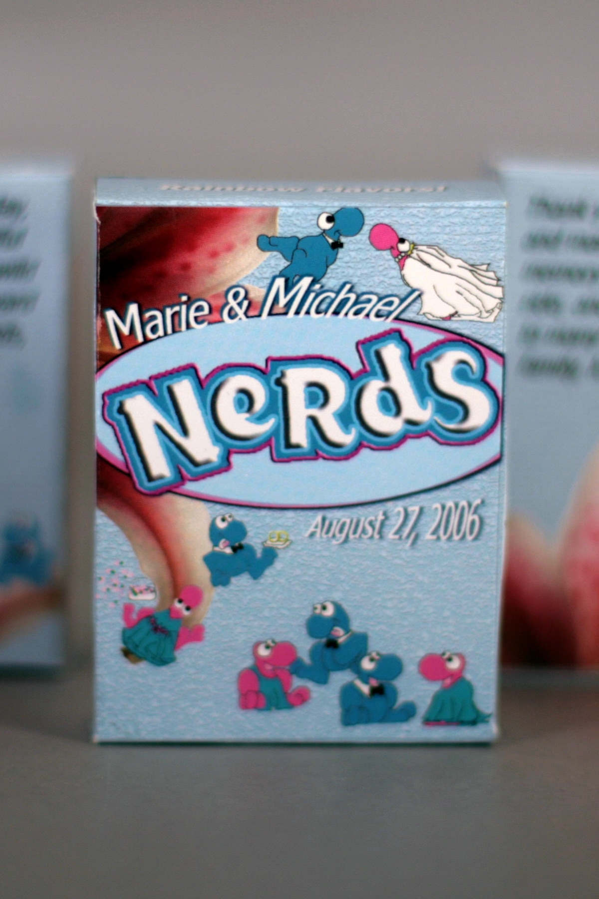 Several customized Nerds Candy Wedding Favor boxes.  They're light blue, with blue and pink Nerds characters, a bride and groom, and stargazer lilies.