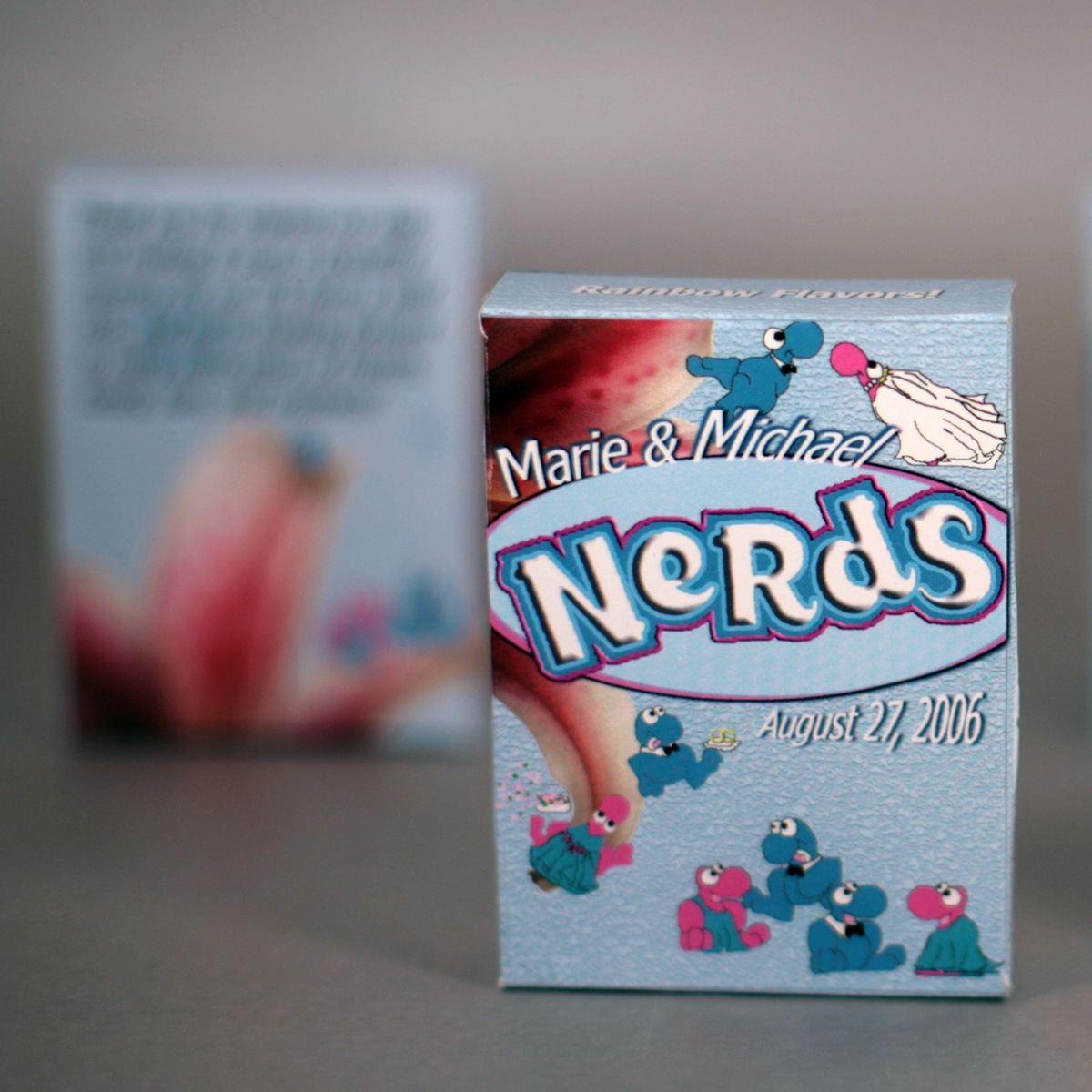 Several customized Nerds Candy Wedding Favor boxes.  They're light blue, with blue and pink Nerds characters, a bride and groom, and stargazer lilies.