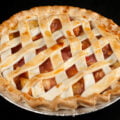 A peach pie with lattice style crust is shown against a black background.