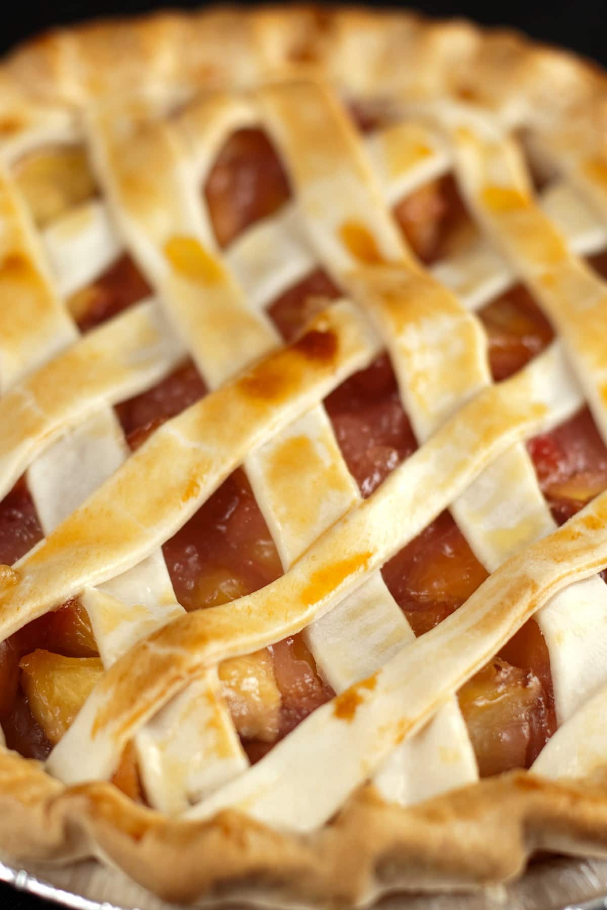 A peach pie with lattice style crust is shown against a black background.