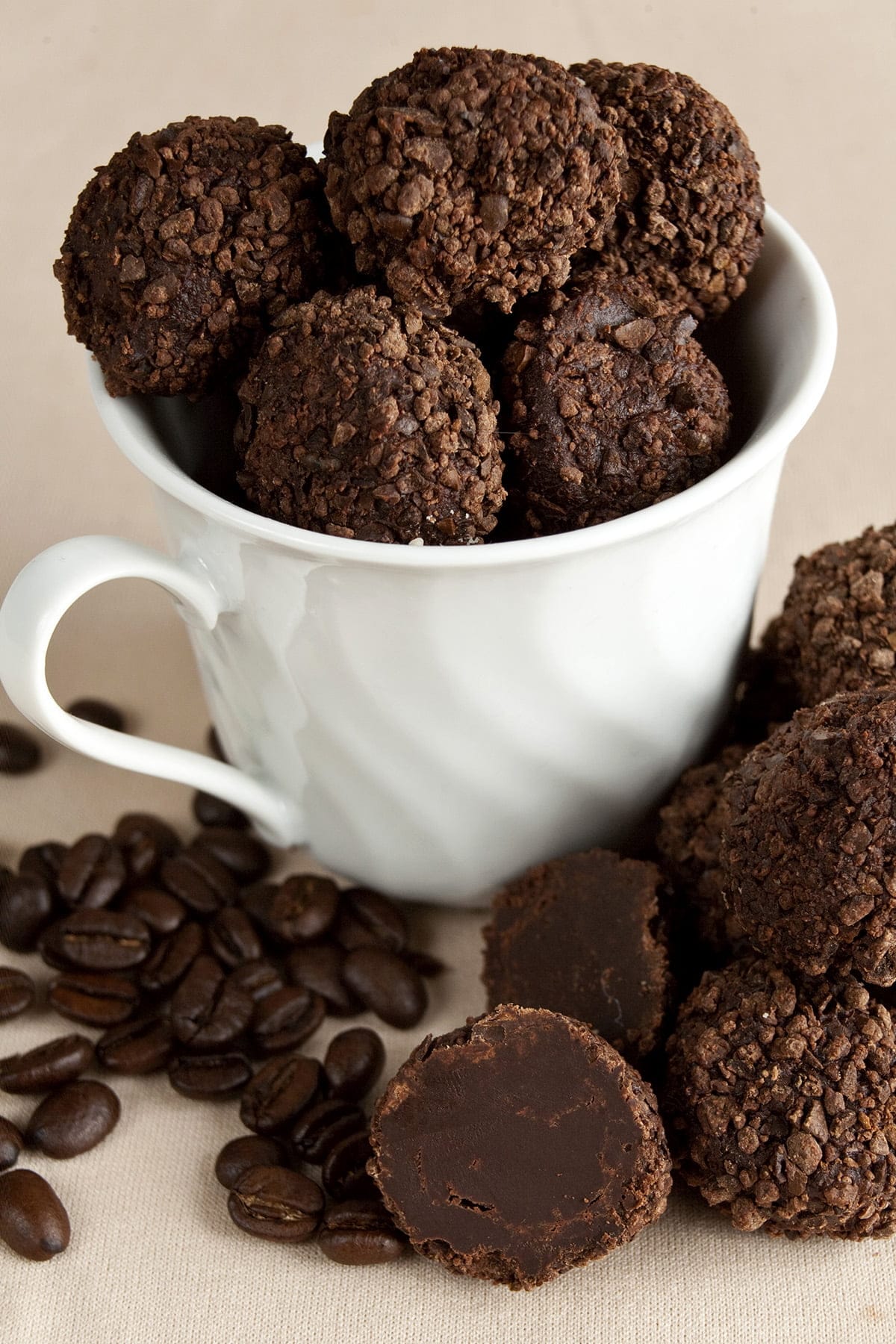 Dark chocolate truffles - coated in smashed coffee beans - fill a white coffee mug. There are stray truffles and coffee beans at the base of the mug.