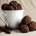 Dark chocolate truffles - coated in smashed coffee beans - fill a white coffee mug. There are stray dark chocolate coffee truffles and coffee beans at the base of the mug.