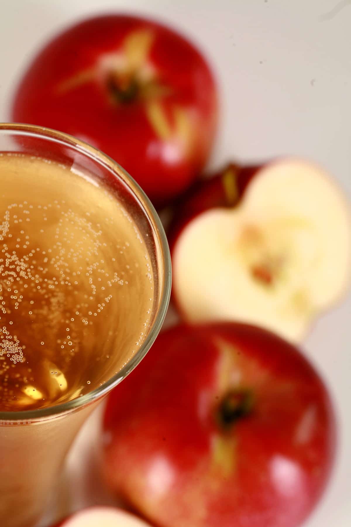 Close of view of a glass of homemade hard apple cider, surrounded by red apples.
