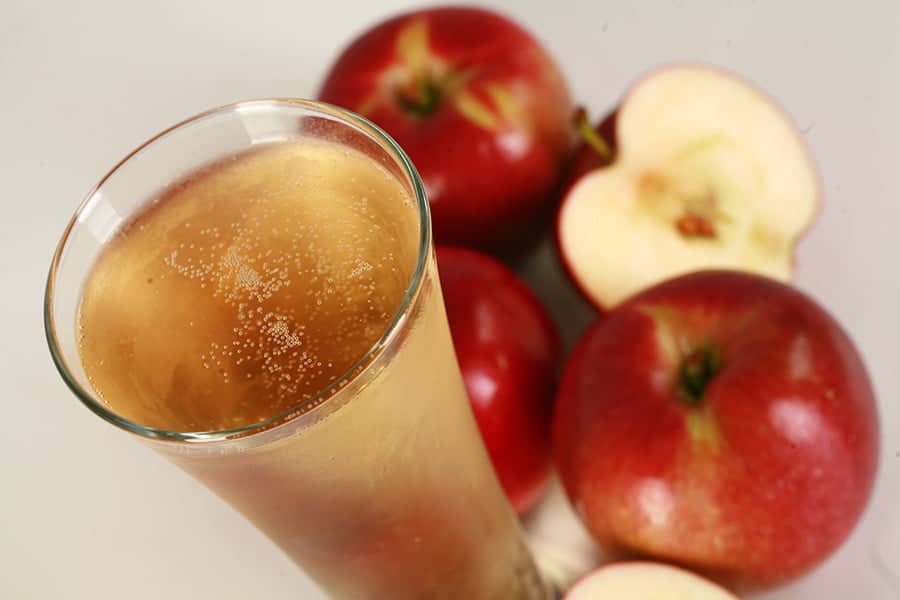 A glass of hard apple cider next to some apples.