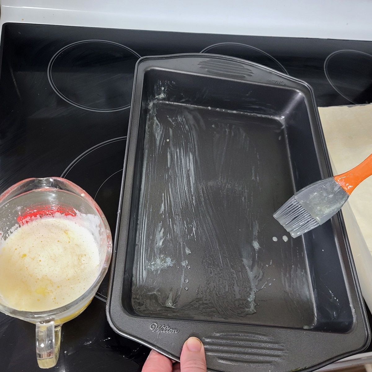 Melted butter is being brushed over the inside of a 9 by 13 baking pan.