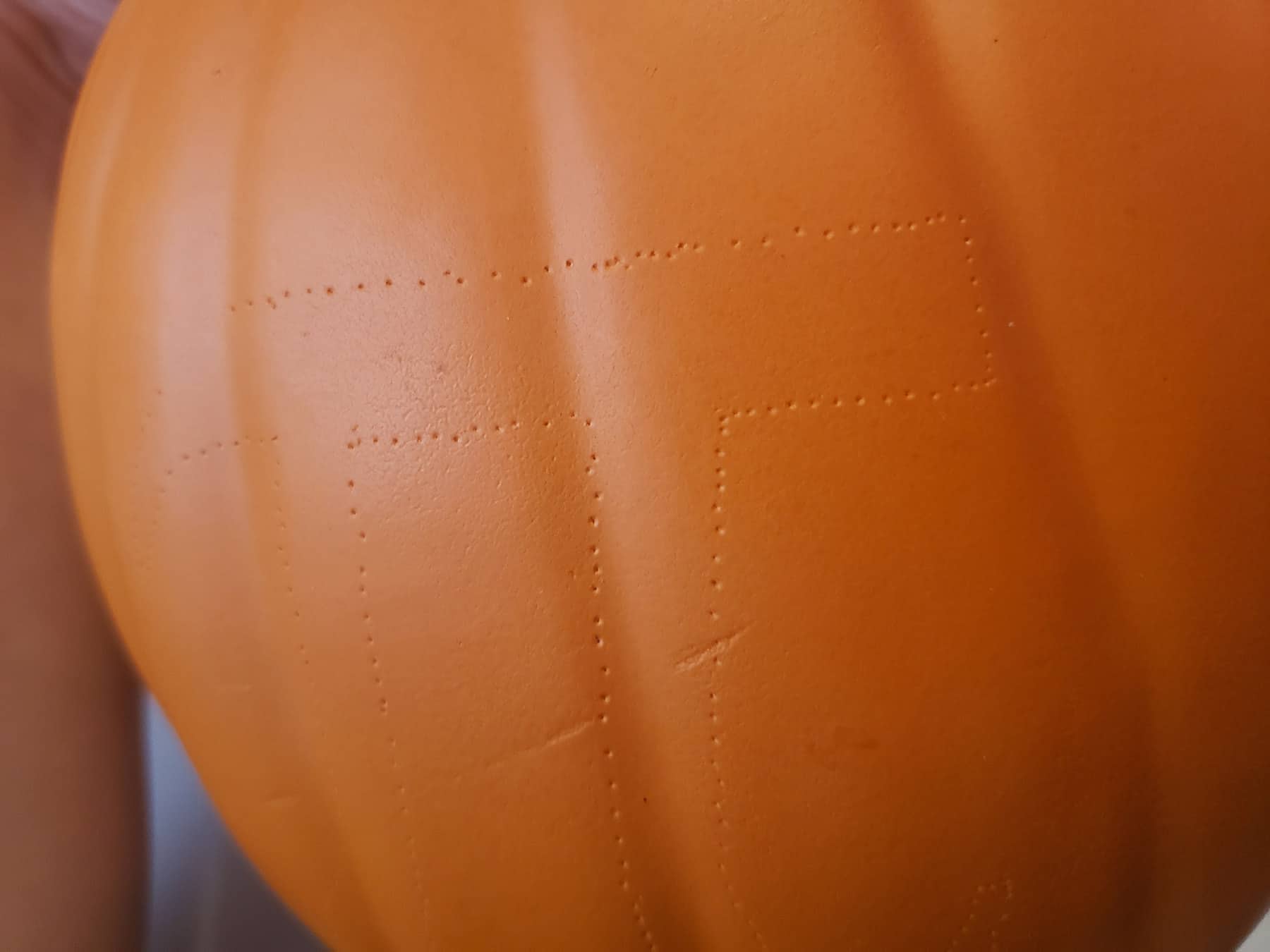 A close up view of a foam pumpkin with a pi symbol traced onto it, via pin pricks.
