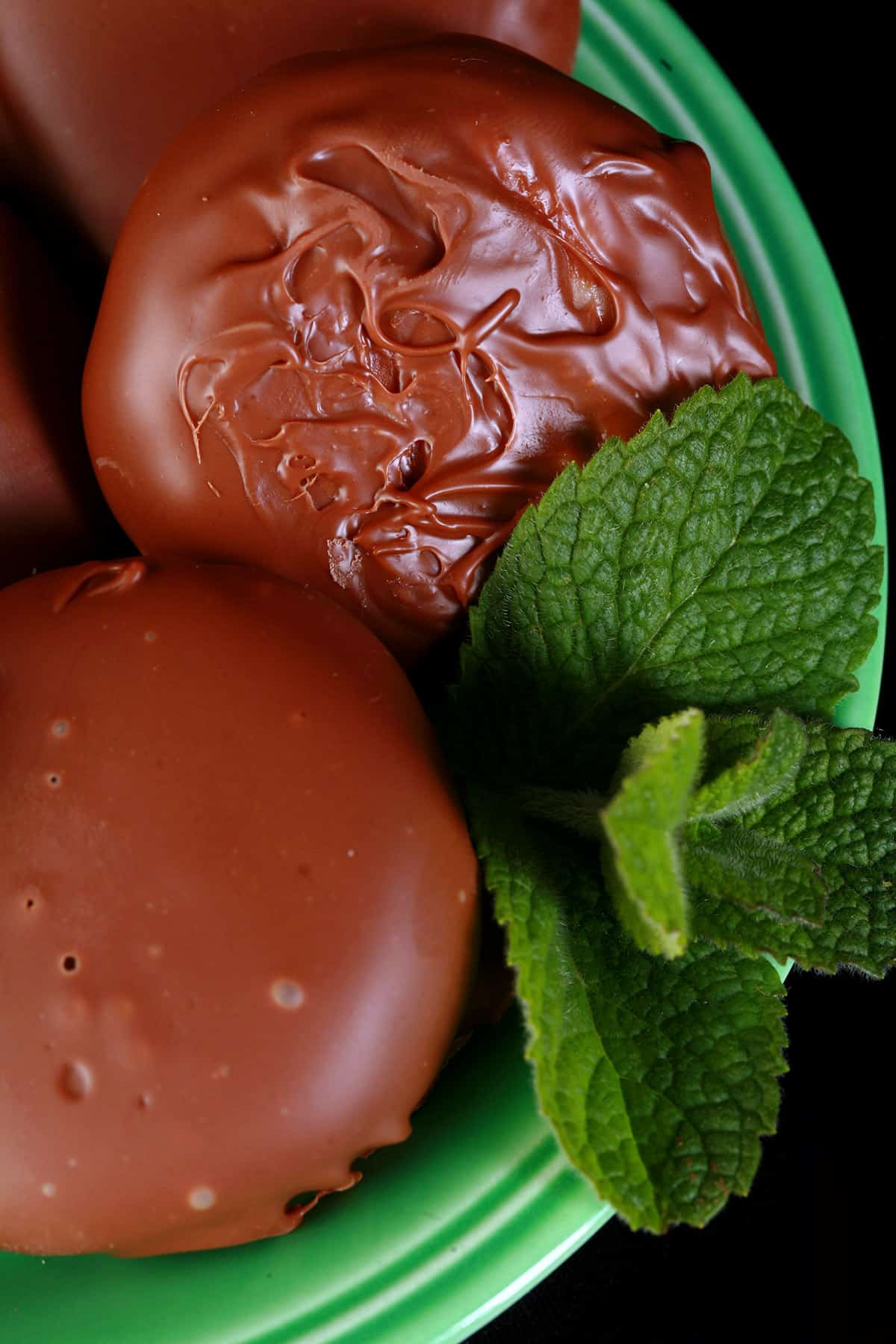 Several homemade peppermint patties on a small green plate, with a sprig of mint.