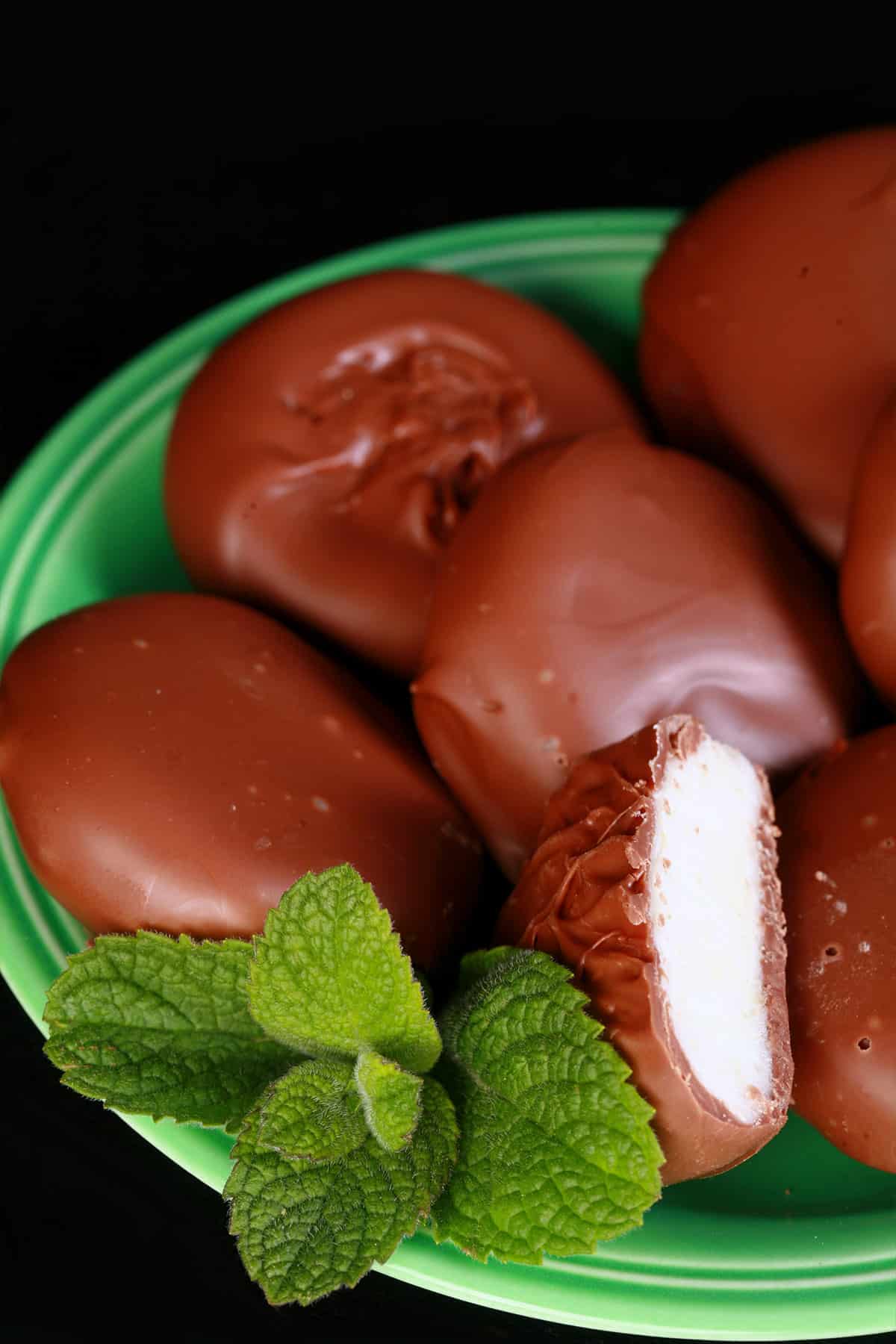 Several homemade peppermint patties on a small green plate, with a sprig of mint.