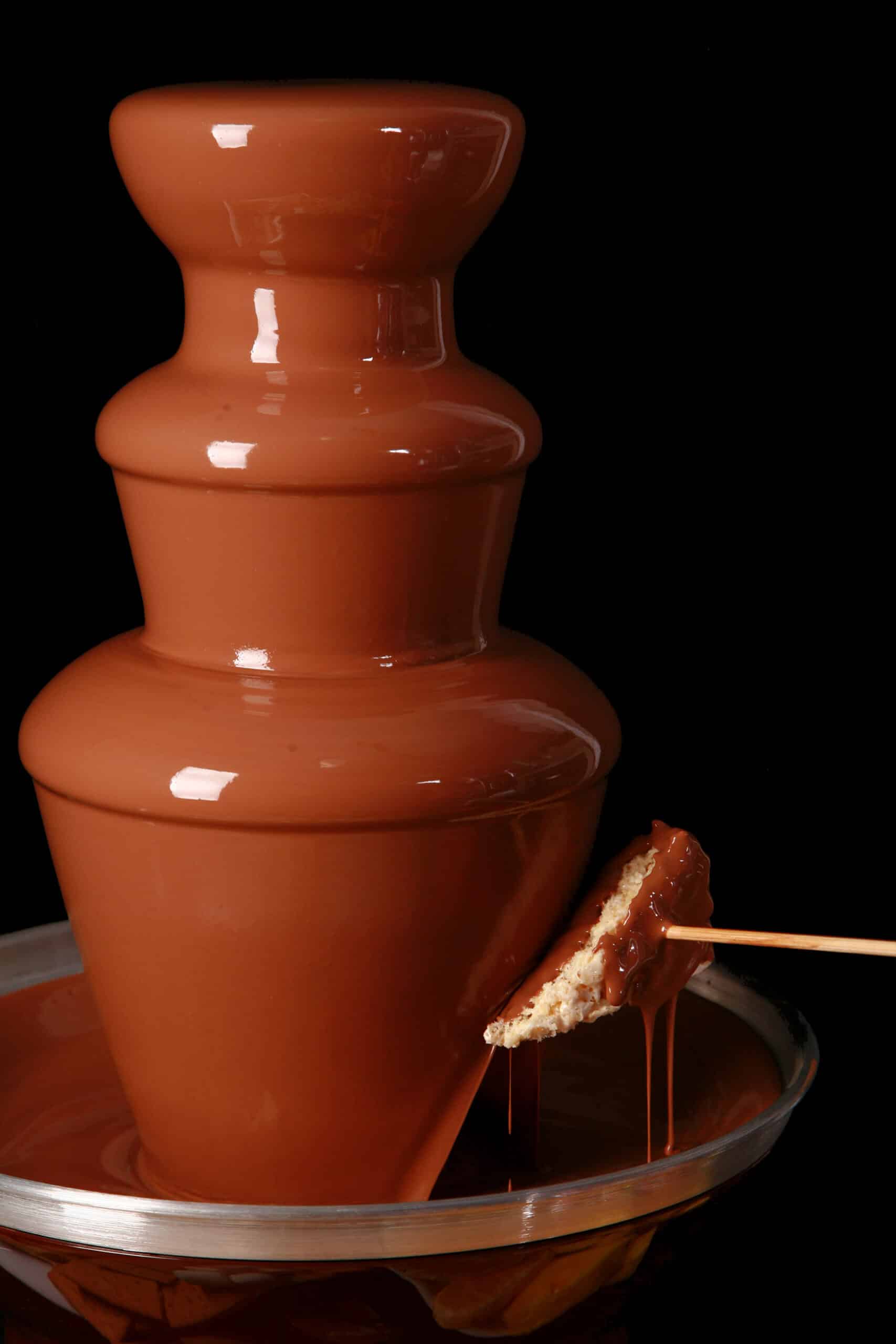 A wedge of rice krispie treat on a skewer, being dipped into a chocolate fountain.