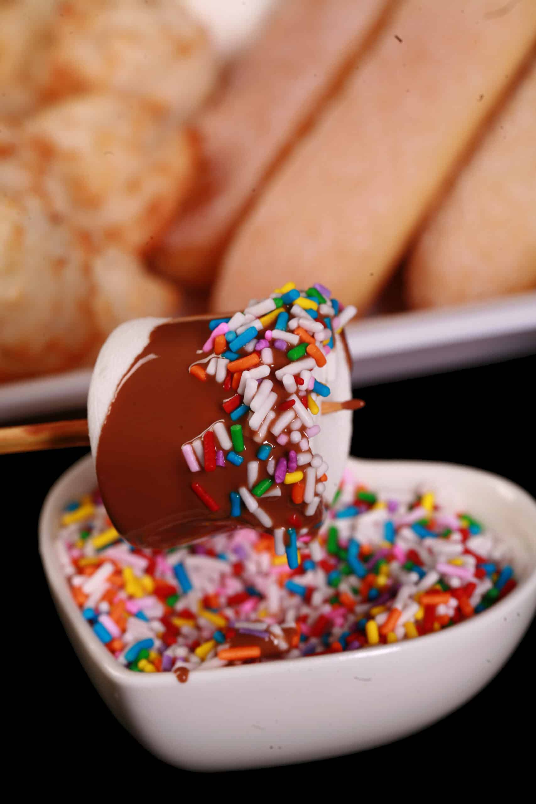 A marshmallow on a skewer, dipped in melted chocolate and coated with multicolored sprinkles.