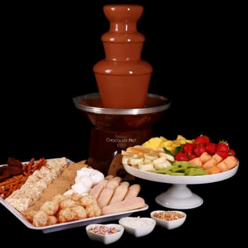 A chocolate fountain in operation, with trays of cookies and fruit laid out in front of it.