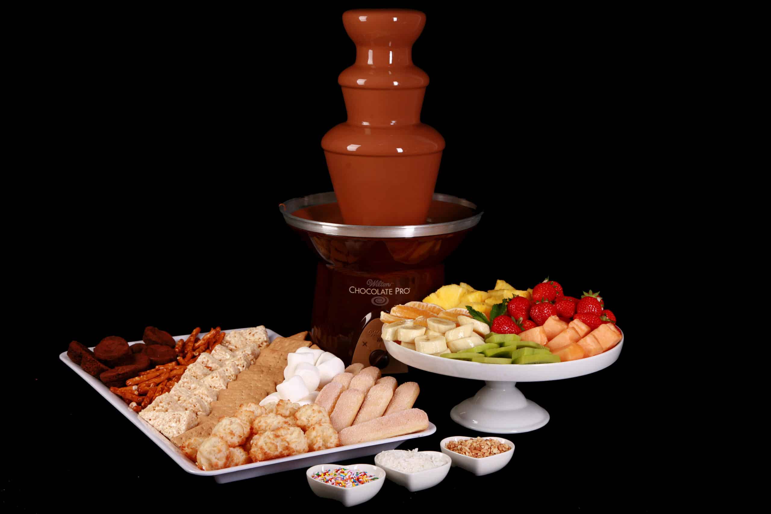 A chocolate fountain in operation, with trays of cookies and fruit laid out in front of it.