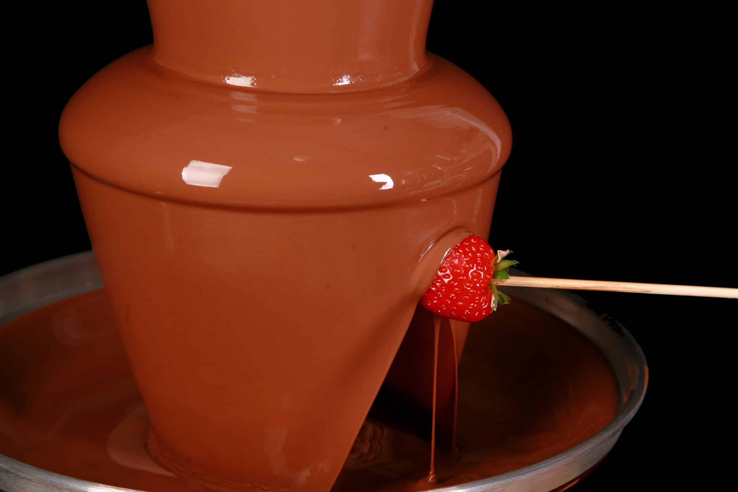 A strawberry on a skewer, being dipped into a chocolate fountain.