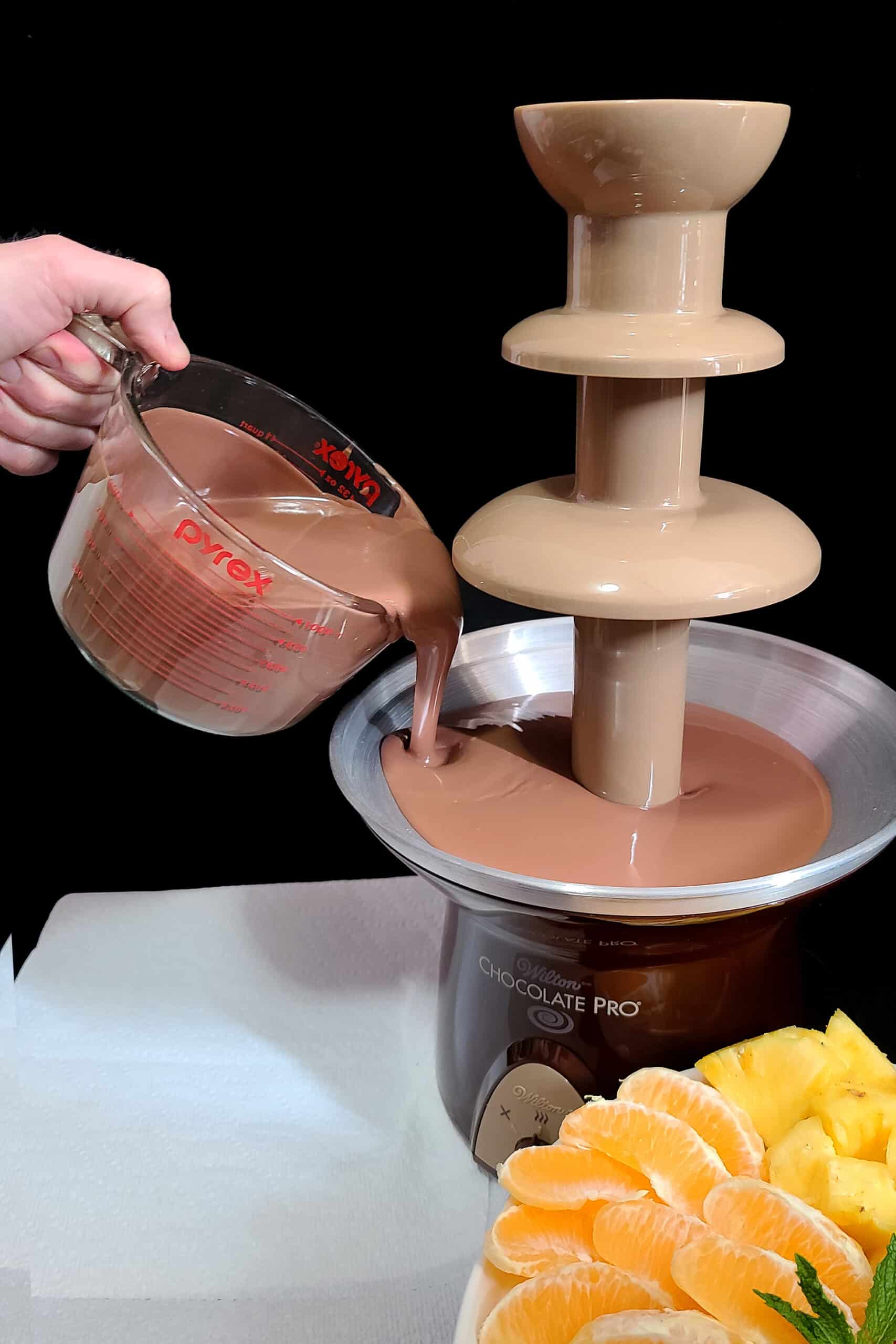 A hand pours melted chocolate mix into a Wilton Chocolate Pro chocolate fountain.