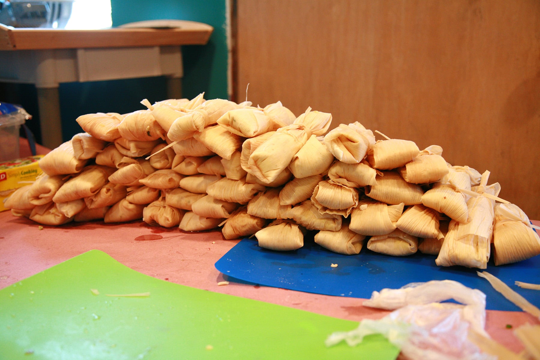 A large pile of wrapped tamales on a work table.