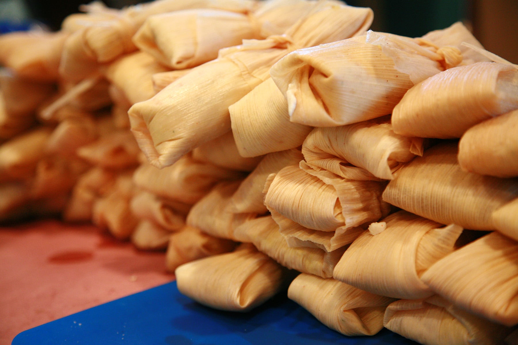 A close up view of a large pile of wrapped tamales on a work table.