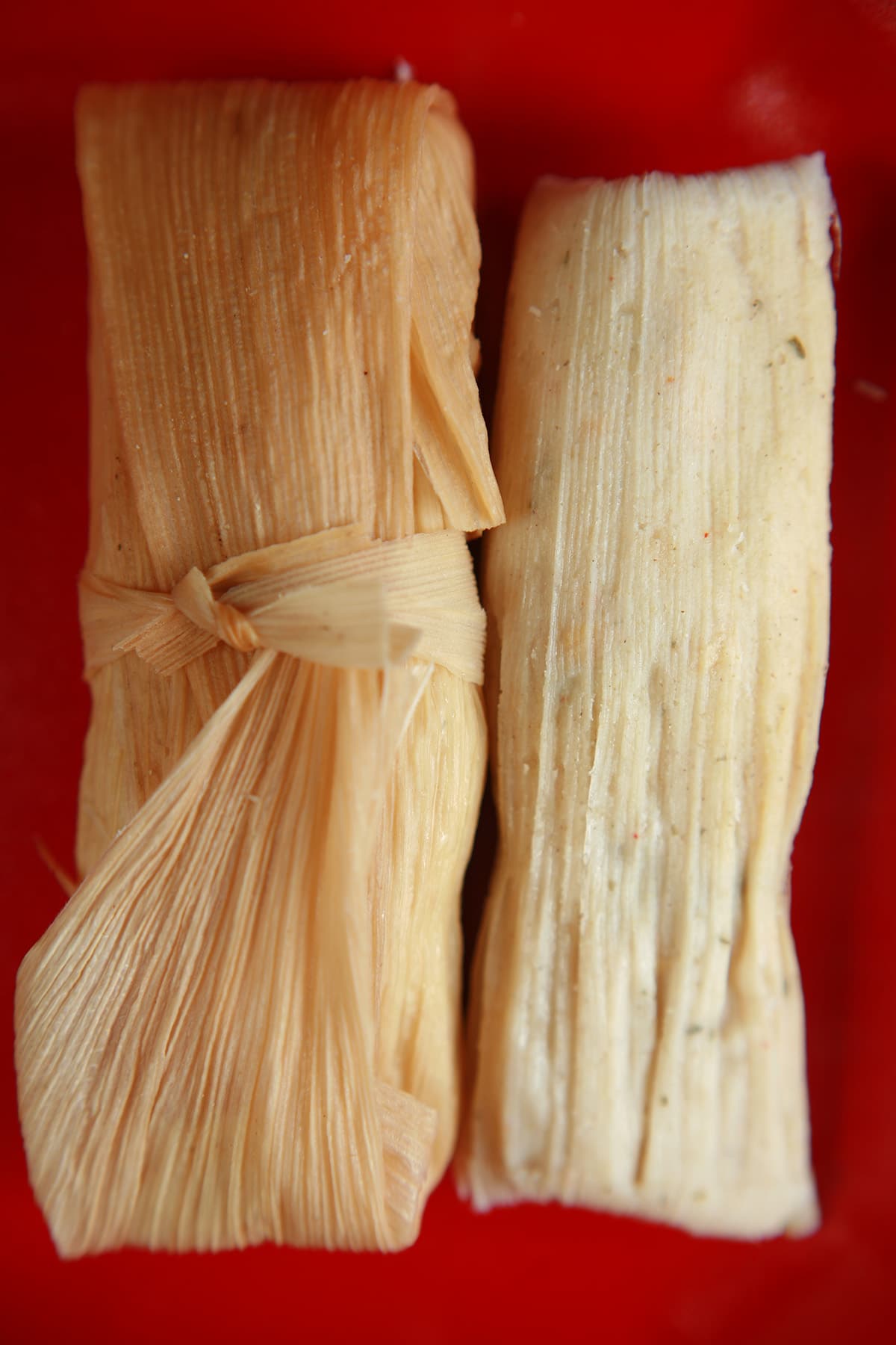 Two salsa verde tamales on a red plate.