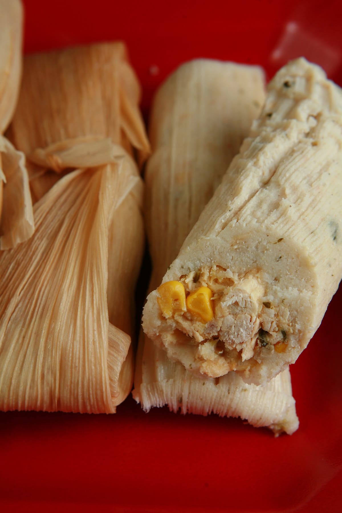 A small pile of salsa verde tamales on a red plate.