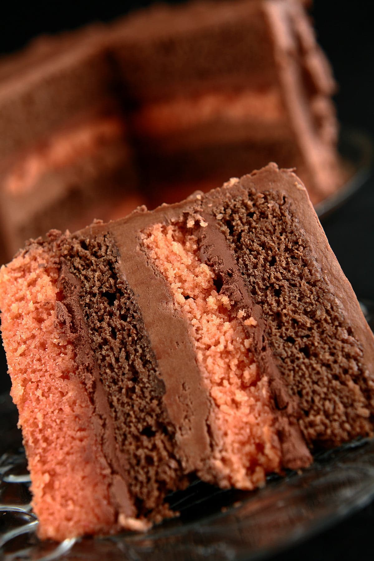 A large slice of B-52 Cake is shown in front of a round, whole cake with a section cut out. The cake shows layers of mocha and orange cakes, separated by layers of blood orange ganache and Irish Cream buttercream.