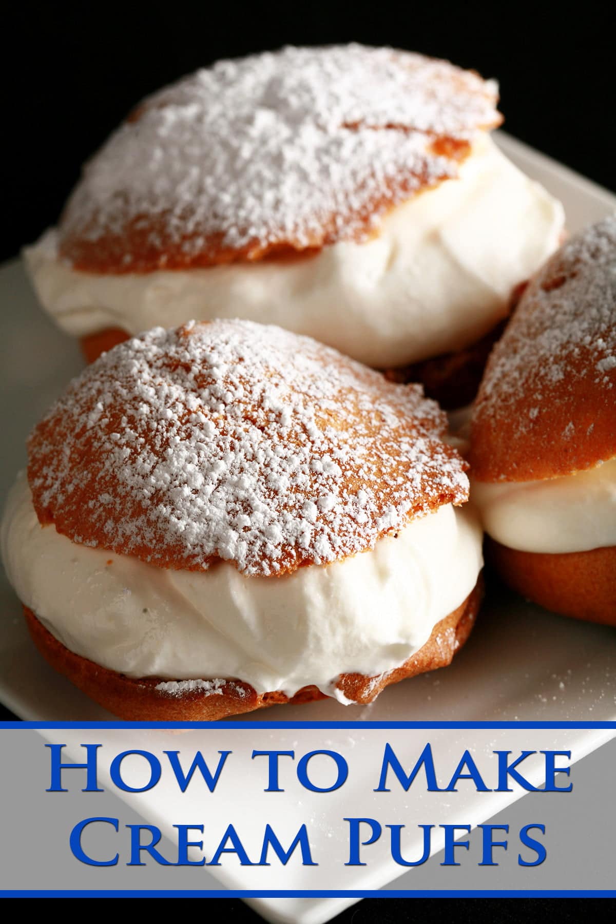 3 Large Cream puffs - with whipped cream in the center, topped with powdered sugar - are pictured on a white plate.