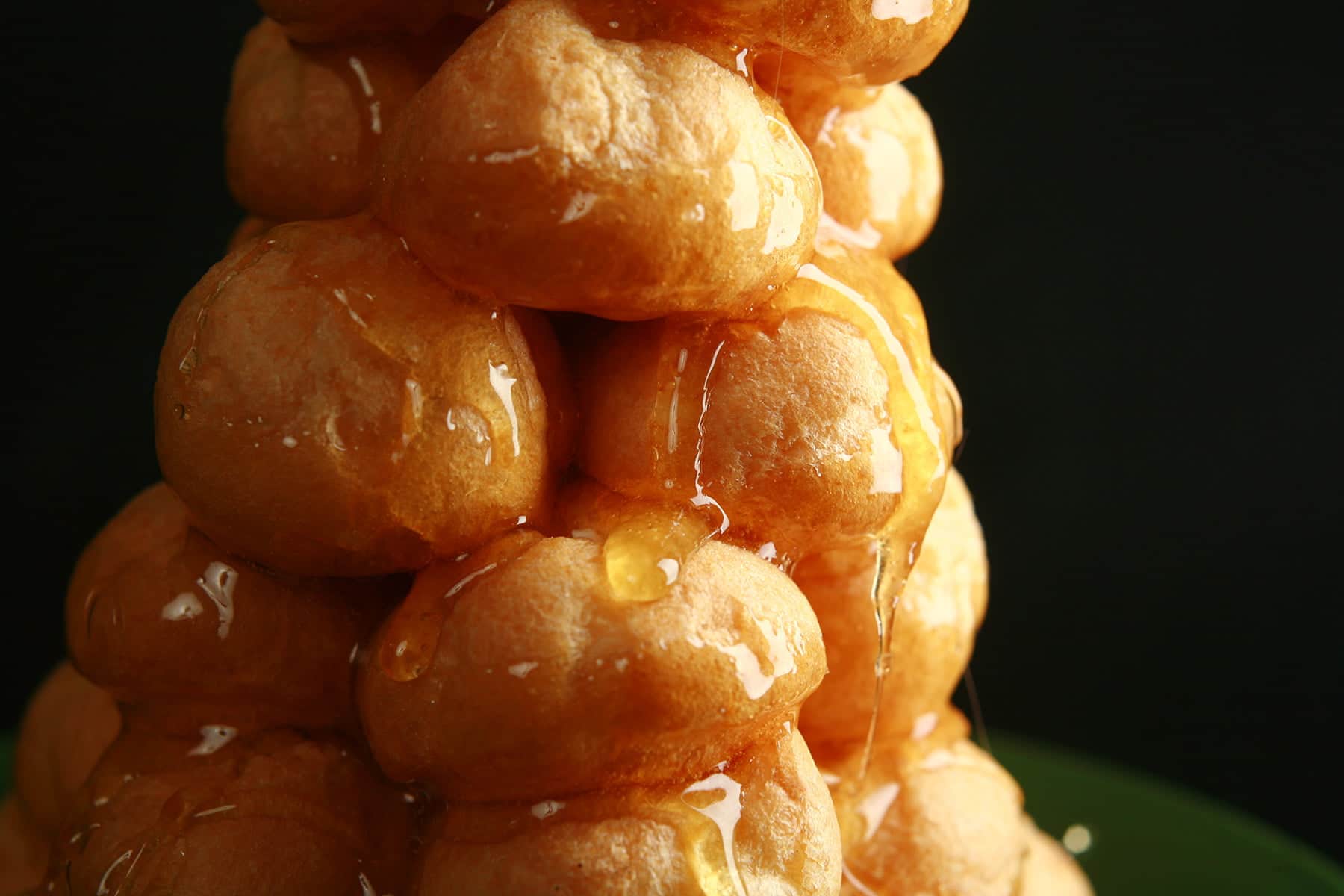 A small croquembouche - a tower made of small cream puffs held together with caramel - is pictured on a small green plate.