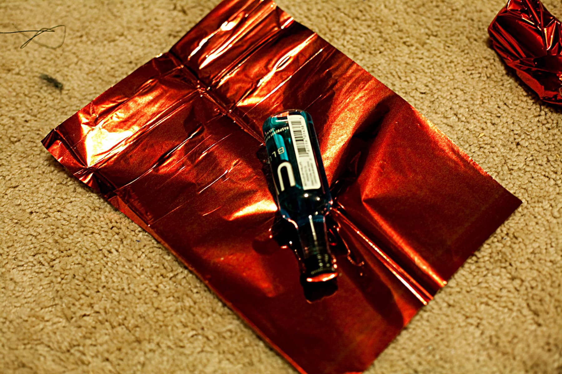 A mini bottle of blue UV vodka is laying on top of a rectangle of red mylar.