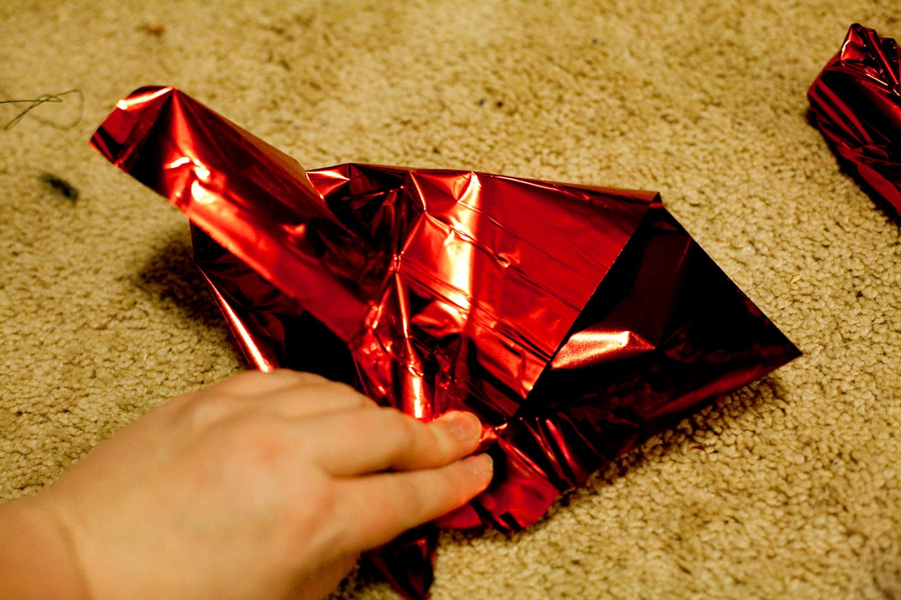 A hand is shown folding a square of red mylar over a mini liquor bottle.
