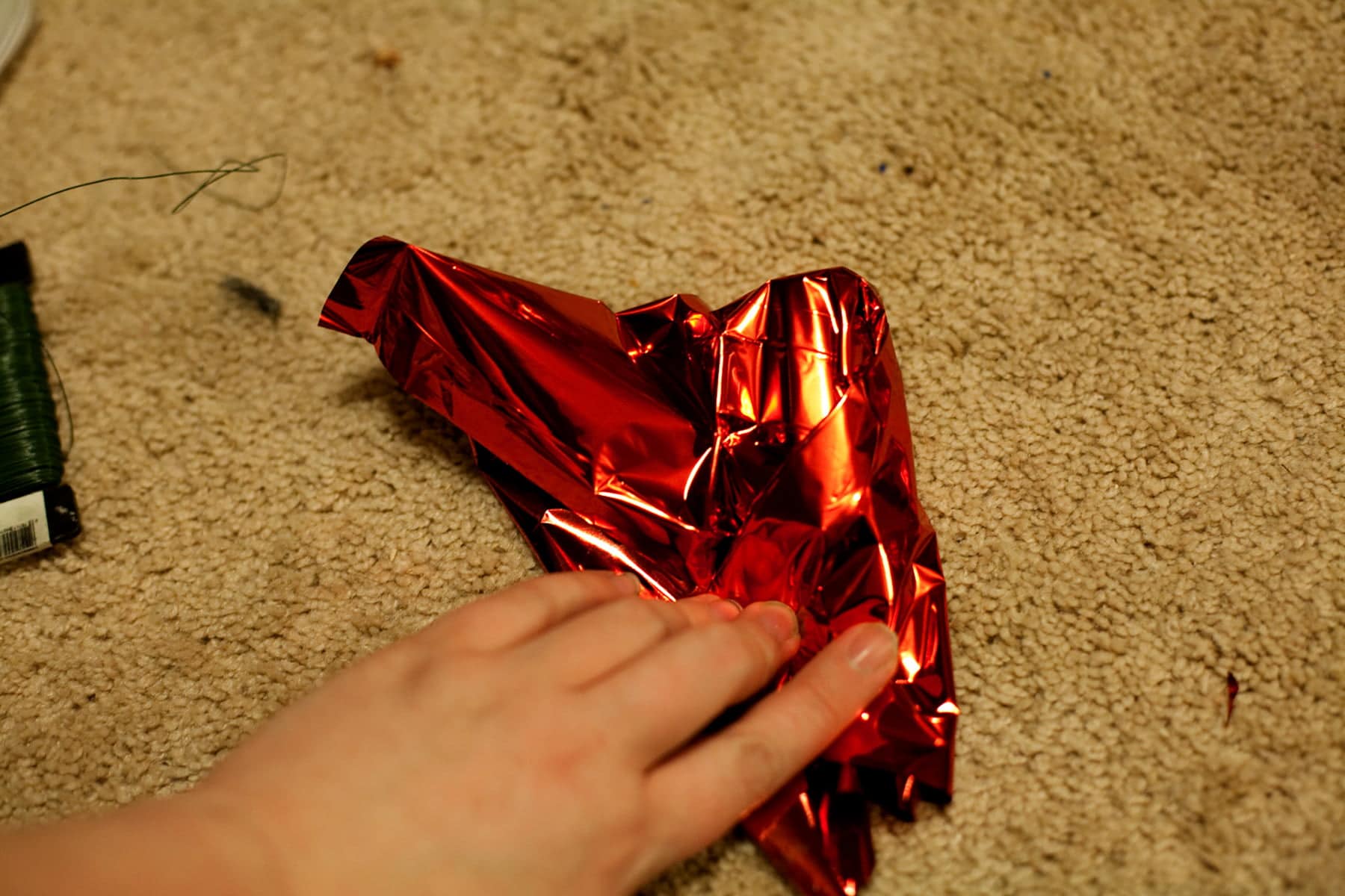 A hand is shown wrapping red mylar tightly around a mini liquor bottle.
