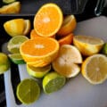 A grouping of lemons, limes, and oranges on a white cutting board. All have been cut in half.