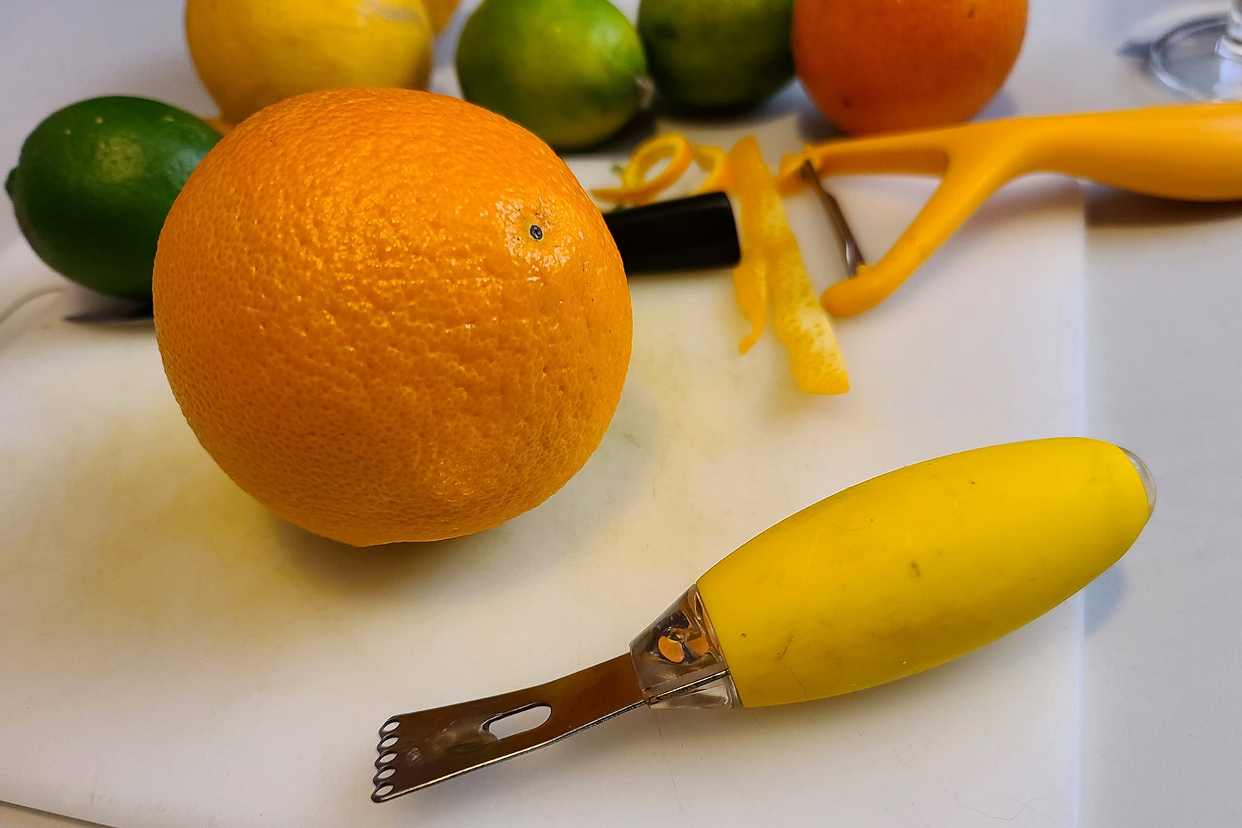 An orange an a channel knife on a cutting board.