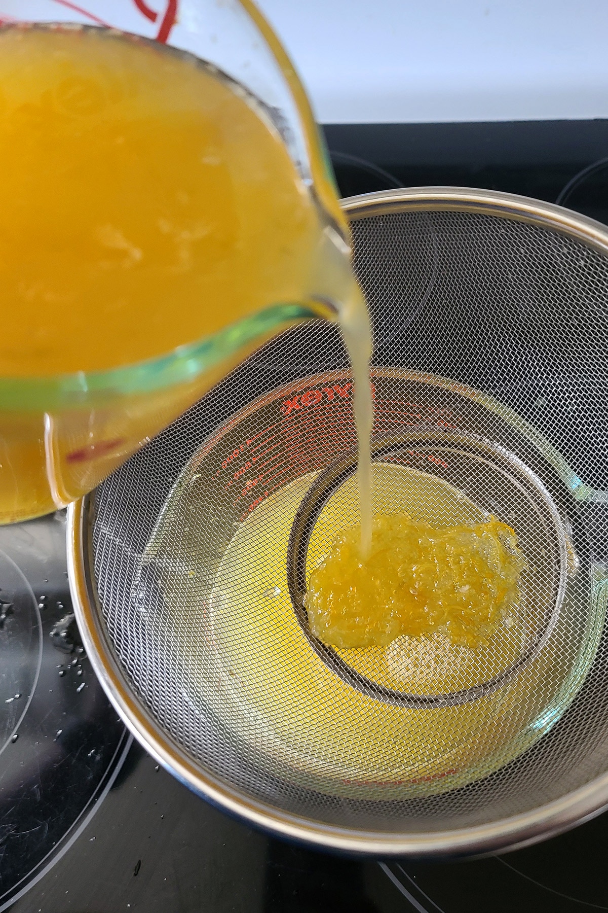 The sour mix being poured through a strainer to remove the zest.