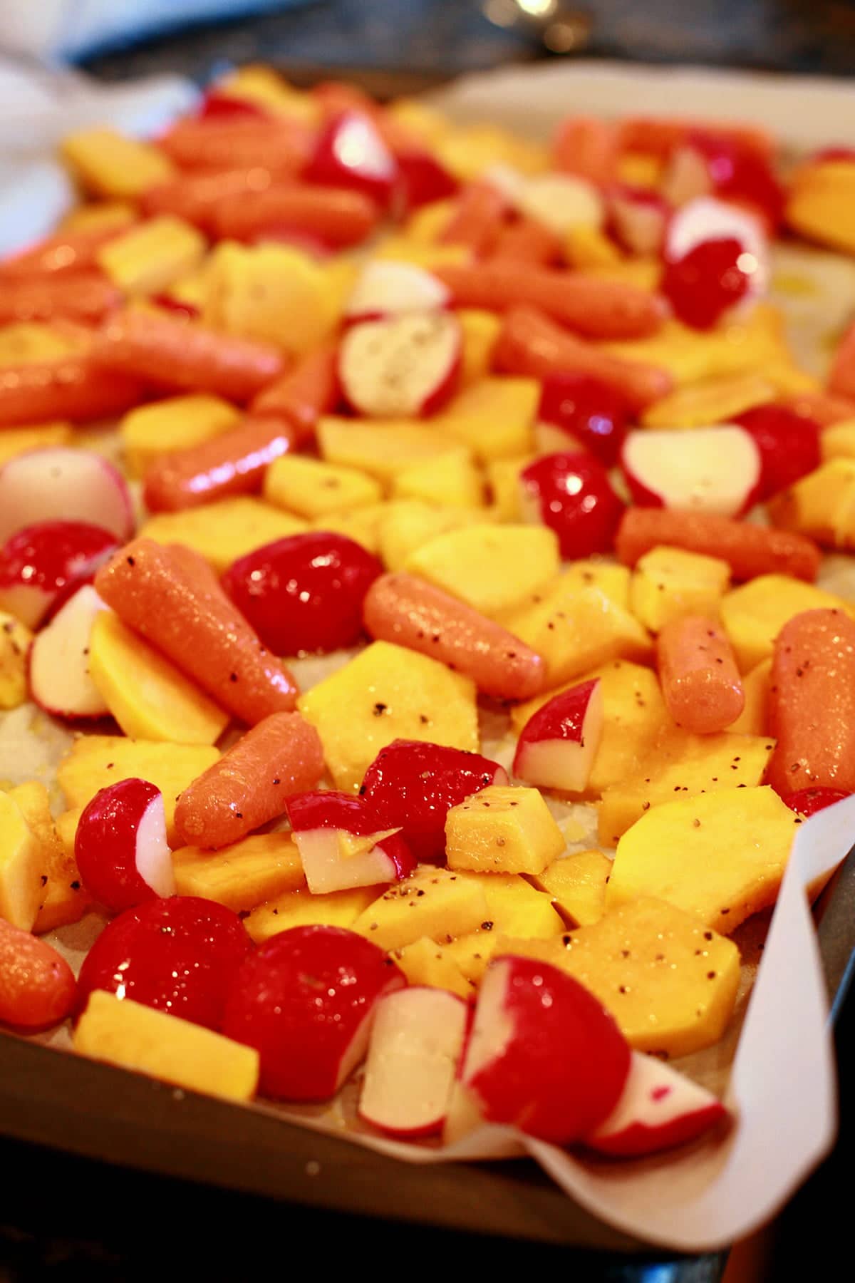 A parchment lined baking sheet is covered with chopped radishes, squash, and baby carrots,