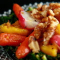 Roasted Radish Salad on a glass plate. Roasted radishes, baby carrots, and squash are served on a base of crispy kale, and topped with a dijon vinaigrette and walnuts.