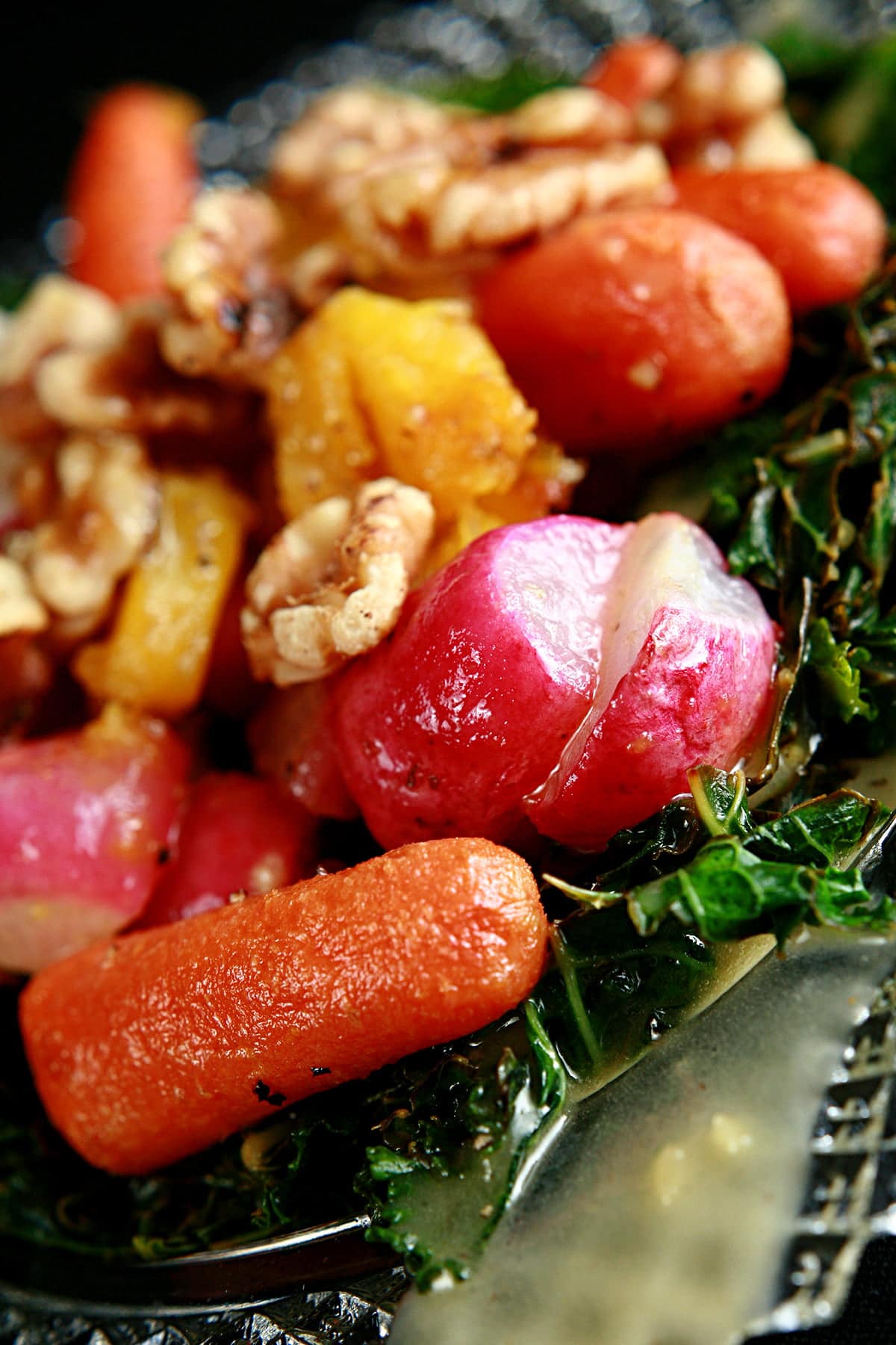 Roasted Radish Salad on a glass plate. Roasted radishes, baby carrots, and squash are served on a base of crispy kale, and topped with a dijon vinaigrette and walnuts.