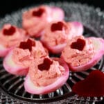 6 pink tie dyed deviled eggs on a glass plate. Each is topped with a heart shaped piece of pickled beet.